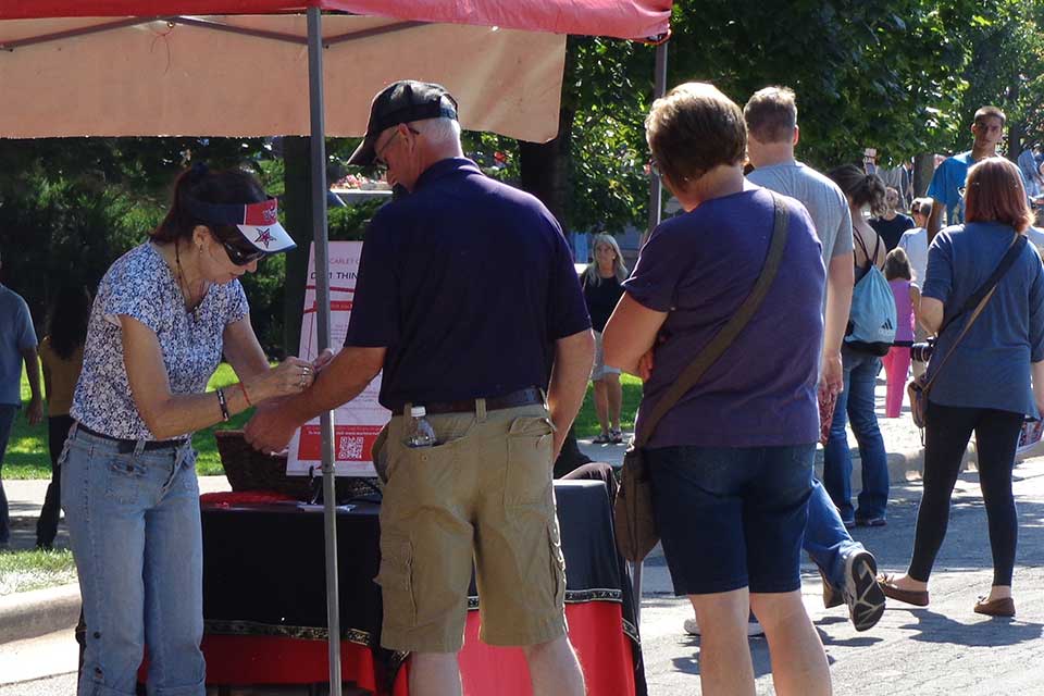 Volunteer tying red bracelet on ArtPrize 2014 visitor