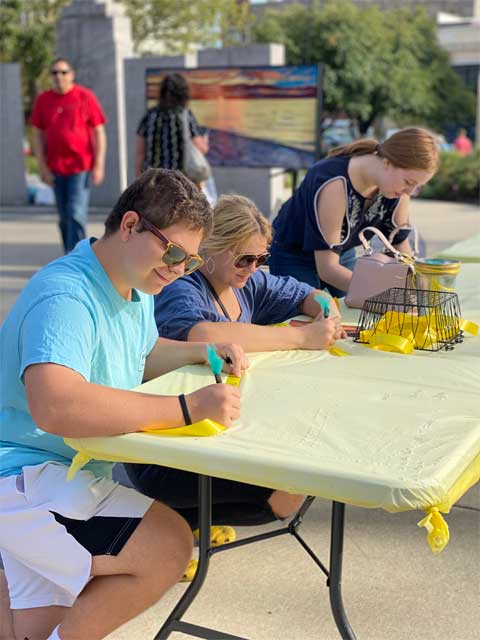 Visitors writing messages on yellow ribbons at the Voices Project during ArtPrize 2021